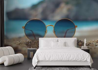 A pair of sunglasses is sitting on the sand at the beach Wall mural