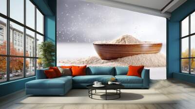  A wooden bowl filled with a heaping pile of nutritious wheat flour with some flour scattered on the table and gray background Wall mural