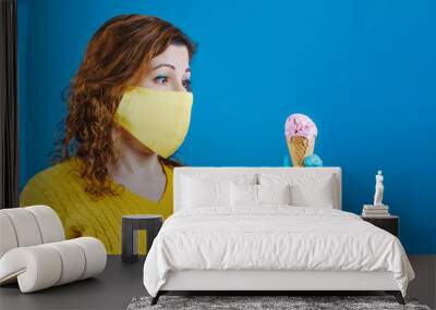 Young woman is sad because the homemade mask she wears doesn't let her eat the ice cream she wants so much. She must protect herself from Covid-19 or Ncov-2019 coronavirus infection. Wall mural