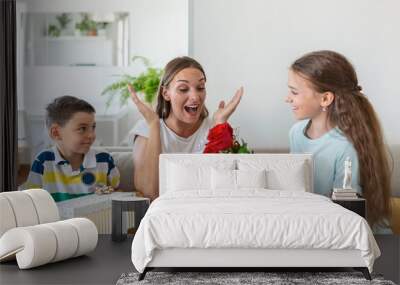 Cheerful little girl with bouquet of roses flowers and youngest brother with gift box smiling and congratulating happy mom on mother day at home. Happy Mothers Day! Wall mural