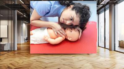 CPR practitioner examining airway passages on infant dummy. Model dummy lays on table and two doctors practice first aid. Wall mural