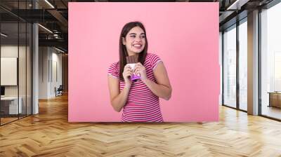 Lovely smiling teenage girl eating chocolate. Image of happy cute young woman standing isolated over pink background eating chocolate. Wall mural