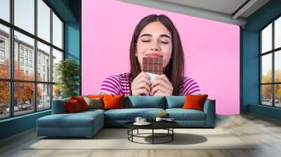 Lovely smiling teenage girl eating chocolate. Image of happy cute young woman standing isolated over pink background eating chocolate. Wall mural