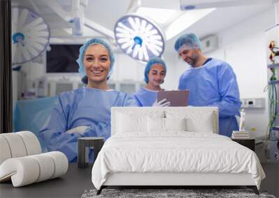 Portrait of female woman nurse surgeon OR staff member dressed in surgical scrubs gown mask and hair net in hospital operating room theater making eye contact smiling pleased happy looking at camera Wall mural