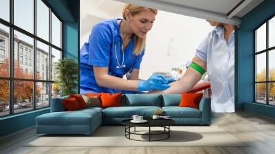 Preparation for blood test with senior woman by female doctor medical uniform on the table in white bright room. Nurse pierces the patient's arm vein with needle blank tube. Wall mural