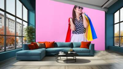 Young attractive girl in sunglasses enjoying a good shopping , with bags in hand. Young happy summer shopping woman with shopping bags isolated on pink background Wall mural