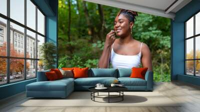 Young happy African woman eating blueberries in green summer garden, looking at camera and smiling Wall mural