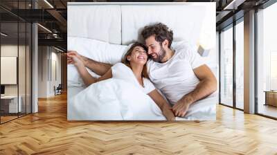 Young loving couple in the bed. Young couple lying in bed and laughing while tickling each other. Happy sensual young couple lying in bed together in the morning Wall mural