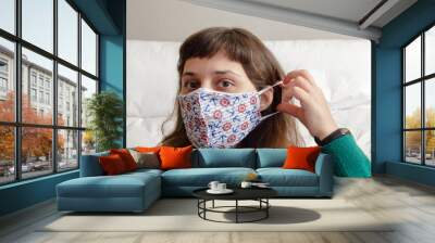 young brunette woman wearing a printed fabric face mask looking to camera Wall mural