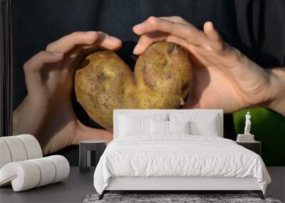 Heart-shaped potato in hands - love hidden in the earth. Two hands on a black background Wall mural