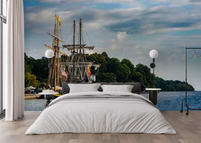 Two Tall Ships moored in a protected harbor with a treed shoreline in the background Wall mural