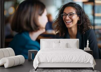 Two professional women engaged in a cheerful discussion over coffee in a cafe setting. Wall mural