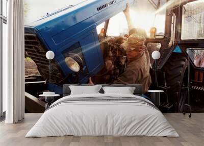 Farmer mechanic repairing blue tractor engine. Repair agricultural technology at sunset. Wall mural