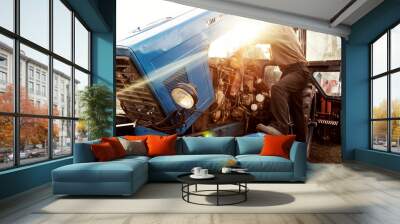 Farmer mechanic repairing blue tractor engine. Repair agricultural technology at sunset. Wall mural