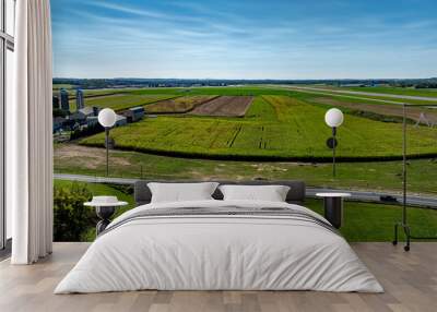 A wide view of lush farmland showcases vibrant green and brown fields, with silos dotting the landscape under a bright blue sky. This serene location reflects rural agricultural life. Wall mural