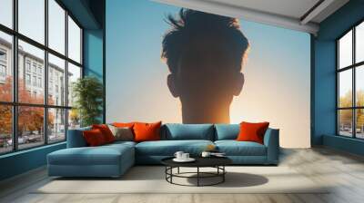 Silhouetted portrait of a person against a vibrant sunset sky. Backlit, with tousled hair and serene atmosphere. Perfect for themes of introspection, tranquility, and natural beauty. Wall mural