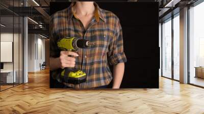 A girl in a work shirt holds a screwdriver in her hands, a symbol of feminism, on a black background Wall mural