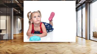 Portrait of a small beautiful girl in a dress lying on the floor and looking up, isolated on a white background Wall mural