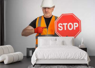 Builder orders to stop. Stop sign in hands of worker. Concept he warns of danger. Builder demonstrates stop sign. To metaphor of danger due to road works. Road worker on gray background. Wall mural