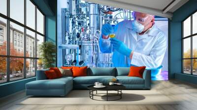 Chemist with a test tube on the background of a laboratory fermenter. Observation of the fermentation process. Laboratory equipment. Experiments in the field of pharmaceuticals. Microbiology. Wall mural