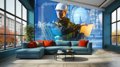 Male technologist at chemical plant. Engineer stands with laptop near factory. Manufacturing technologist. Technologist near tanks with cryogenic liquid. Factory contractor in uniform Wall mural