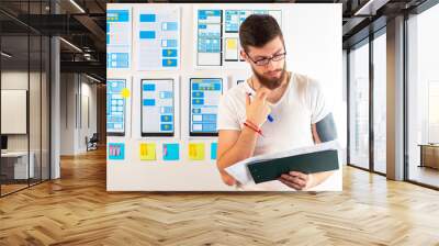 Male UI UX designer. Bearded man next to the dialog box templates. Man develops the design of mobile app. Web design, user interface of programs. Project of a mobile application for an online store. Wall mural