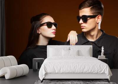 Portrait of a guy and a girl in sunglasses. Man and woman in black clothes. Young guy and girl are posing. Young couple on a dark background. Portrait students in sunglasses close up. Wall mural