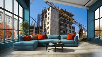 Scenery with buildings under construction. Crane boom over construction site. Erection of multi-storey buildings. Process of building houses with residential apartments. Erection monolithic buildings Wall mural