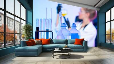 Table in a chemical laboratory on the background of a girl with a test tube in her hands. The girl is conducting a study of a yellow chemical liquid. Quality control of products. Wall mural