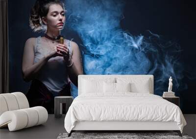 Vaper girl thought about something. Woman holds a vape device. Lot of smoke next to vaper. Clouds of steam from vape device. Female student with e-cig with a pensive look. Reflections. Stress removal Wall mural