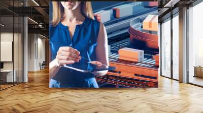 Woman manager of manufacturing company. Conveyor line behind girl. Lady with tablet tracks boxes on conveyor belt. Automated warehouse manager. Cropped female supervisor stands near conveyor belt Wall mural