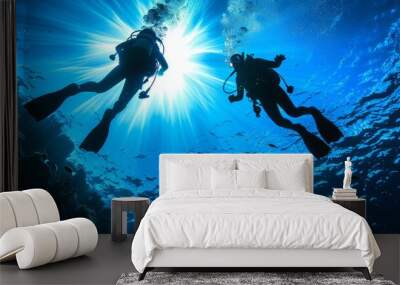 Two scuba divers swimming in the ocean with sun shining through the water Wall mural