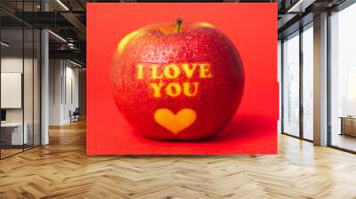 Valentine's Day themed apple with I Love You message and a heart symbol covered in water droplets and placed on a red background Wall mural