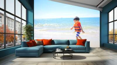 Asian baby boy with swimwear and life vest walking on the tropical beach . Wall mural