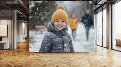 Happy child enjoying a snowy winter day, dressed in a warm coat and beanie, with snowflakes falling and family walking in the background, joyful seasonal outdoor adventure Wall mural