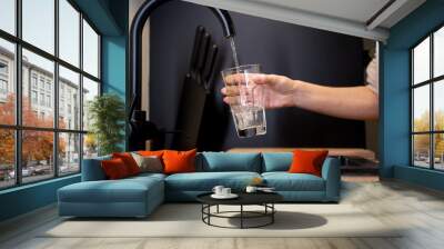 Close-up of a woman's hands pouring a glass of fresh water from the tap in the kitchen. Woman drinking a glass of water. Wall mural