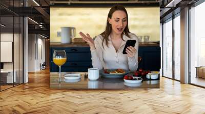 happy beautiful young woman in the kitchen with her phone, playing online games, wins a prize. he sh Wall mural