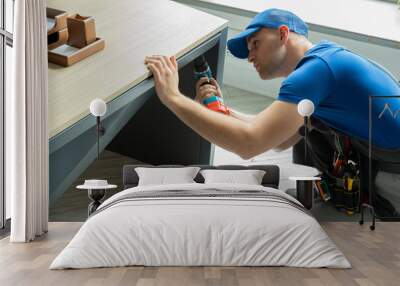 Male handyman using an electric screwdriver tool in his hand and repairing a wooden table Wall mural