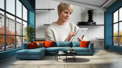 Portrait of a smiling Caucasian middle-aged woman sitting in an armchair, using a modern tablet gadget, communicating online Wall mural