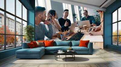 Achieving success together. Group of young modern people in smart casual wear discussing something and smiling while working in the creative office Wall mural