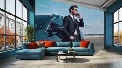 Always available. Handsome young businessman talking on the phone while standing near his car outdoors Wall mural