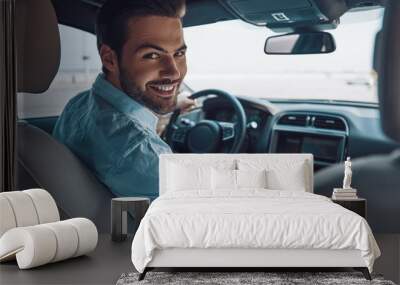 Are you ready to go? Rear view of young man in smart casual wear looking at camera over shoulder and smiling while driving a status car Wall mural