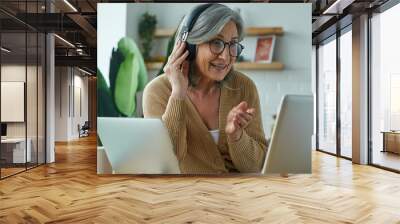 Cheerful senior woman looking at laptop and gesturing while working from home Wall mural