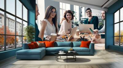 Colleagues become friends. Group of young modern people in smart casual wear discussing something and smiling while working in the creative office Wall mural