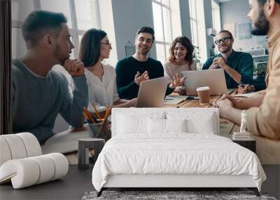 Confident and smart. Group of young modern people in smart casual wear discussing something and smiling while working in the creative office Wall mural