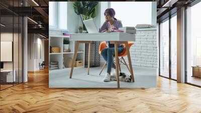 Confident young woman with purple hair working on laptop while sitting at her working place Wall mural