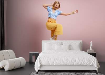 Full length of fashionable young woman dancing and smiling against color background Wall mural