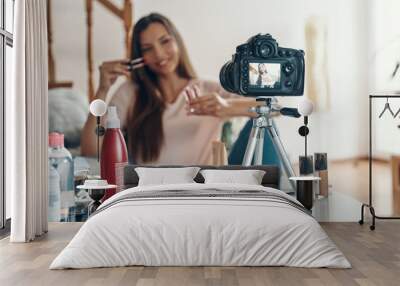 Good looking young woman applying lip gloss and smiling while making social media video Wall mural