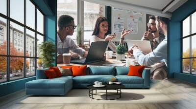 Group of young people discussing business together while having meeting in the office Wall mural