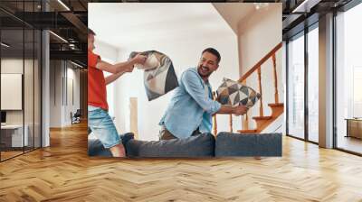 Happy young father and son having pillow fight and smiling while spending time at home Wall mural